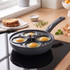 Non-stick frying pan with four-egg poacher insert on hob, eggs cooking