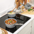 Set of grey non-stick pans and cookware with food, shown on a kitchen surface