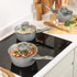Set of three grey non-stick saucepans with lids on kitchen hob and worktop