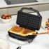 Square waffle maker open with two cooked waffles inside, on kitchen countertop.
