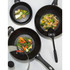 Set of three black non-stick woks with assorted stir-fried vegetables, shown from above.