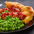 Plate of sausages with Yorkshire pudding and green peas, traditional British meal.