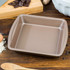 Brown non-stick square baking tin on wooden surface with baking ingredients
