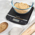 Digital kitchen scale in black with bowl of mixed fruit, display shows 176 grams