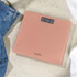 Person in white trainers and jeans standing on pink bathroom scale