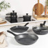 Set of black and white non-stick pans and pots with food on a kitchen worktop