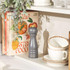 Grey Salter pepper mill on kitchen shelf beside cookbooks and stacked cups