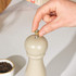 Cream pepper mill, hand adjusting top, with bowl of peppercorns beside