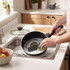 Washing a black non-stick saucepan in kitchen sink with sponge, showing easy cleaning.