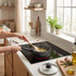 Person stirring food in black saucepan on modern induction hob in bright kitchen