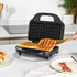 Black sandwich and waffle maker with interchangeable plates, shown making two golden waffles on a kitchen worktop.
