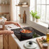 Black saucepan on hob cooking tomato vegetable stew, wooden spoon stirring.