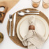 Table setting with cream stoneware plates, stainless steel cutlery and linen napkin on woven placemat