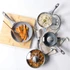Grey speckled saucepan and frying pan set with glass lids, kitchen background