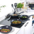 Set of non-stick black frying pans and wok on kitchen hob, cooking assorted dishes.