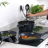 Set of black non-stick pots and frying pans on induction hob, cooking vegetables and steak