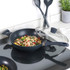 Non-stick black wok with glass lid on hob, cooking stir-fry with vegetables and chicken
