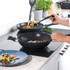 Black non-stick wok on hob with vegetable stir-fry being served onto a blue plate