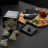 Black tea tin with pyramid tea bags, mint leaves, and glass cup of tea on wooden board