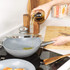 Grey non-stick wok with glass lid shown on a kitchen hob