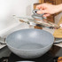 Grey non-stick wok with glass lid shown on a kitchen hob