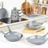 Grey non-stick frying pan on hob, oil being poured in, wooden chopping board beside