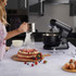 Black stand mixer on kitchen counter with cake, eggs, and baking tools.