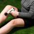 Person using white massage gun on thigh, outdoors on grass