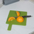 Knife slicing orange on green chopping board