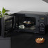 Black microwave oven on countertop, door open, with bowl of soup inside