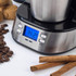 Stainless steel digital coffee grinder on white surface with cinnamon sticks and cookies.