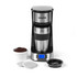 Single-serve silver coffee maker with travel mug, coffee grounds, and coffee pods shown.