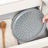 Grey perforated pizza tray shown in kitchen drawer, hand placing tray inside.