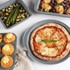 Margherita pizza on grey baking tray with roasted vegetable and chicken dishes nearby