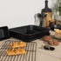 Set of black non-stick baking trays on kitchen counter with cooling rack and pastries.