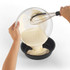 Pouring cake batter from glass bowl with whisk into round non-stick baking tin