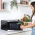Woman using Salter air fryer oven in modern kitchen with a tray of cooked chicken and chips.