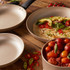 Set of beige non-stick frying pans on wood table, one with omelette and toppings