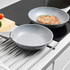 Set of two grey non-stick frying pans, one with steak, on modern kitchen hob.