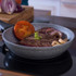 Grey frying pan with cooked steak, tomato, mushrooms, and red onion on a hob