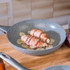 Non-stick frying pan with two bacon-wrapped chicken breasts on sliced potatoes