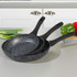 Set of three non-stick speckled frying pans with black handles on kitchen worktop
