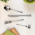 Four-piece stainless steel cutlery set on light wood table, includes knife, fork, spoon and teaspoon.