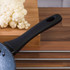 Non-stick frying pan handle in foreground with cauliflower on wooden chopping board