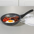 Grey non-stick frying pan with fried egg, bacon and tomatoes on a kitchen counter