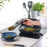 Black frying pan on hob with person serving pesto pasta into blue bowl