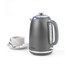 Grey electric kettle with side handle, shown next to cup of tea with lemon slice.