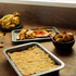 Baking tray with roasted vegetables and chicken, bowl of roast potatoes, dessert in tray.