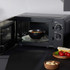 Black microwave oven with open door, heating soup bowl on glass turntable, kitchen setting
