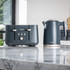 Grey metal tea and coffee canisters with matching kettle pouring hot water into glass mugs